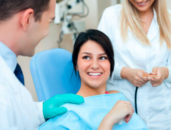 Eine Patientin im Mittelpunkt der Behandlung zwischen Zahnarzt und Zahnarzthelferin, die sich Zeit für ein Gespräch mit der Patientin nehmen.